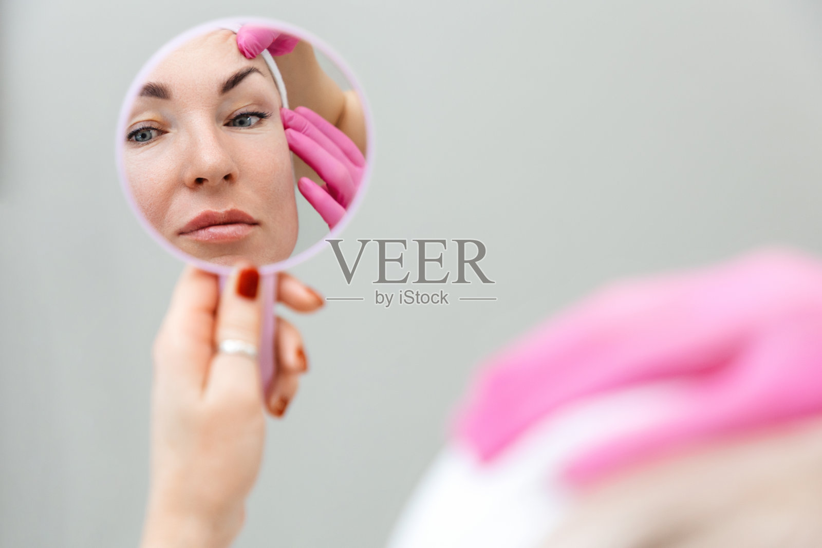 美容整形外科。一个女人在镜子里看着自己的倒影。美容师抿着顾客的眉毛照片摄影图片