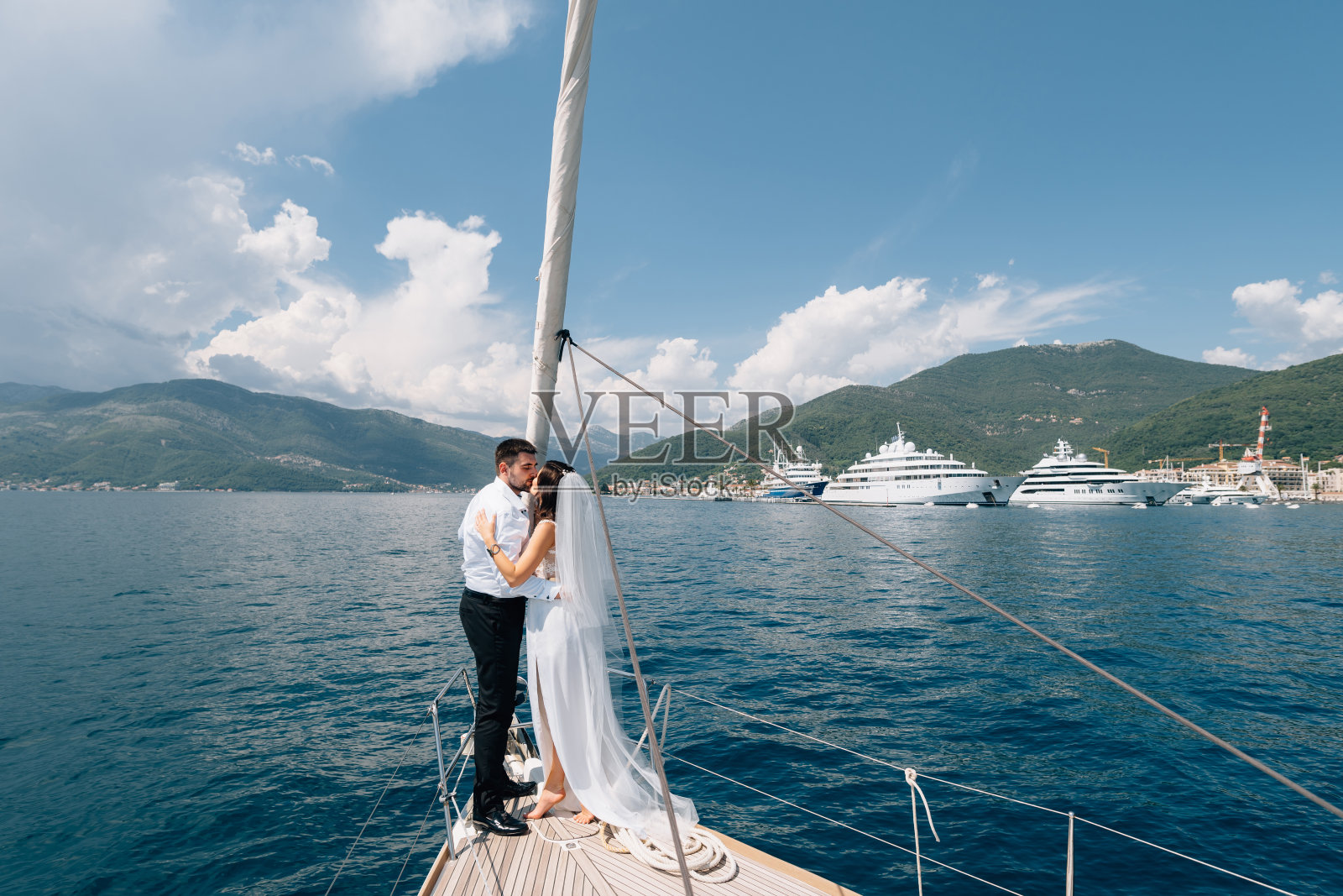 新娘和新郎站在科托湾一艘白色游艇的船头上拥抱照片摄影图片