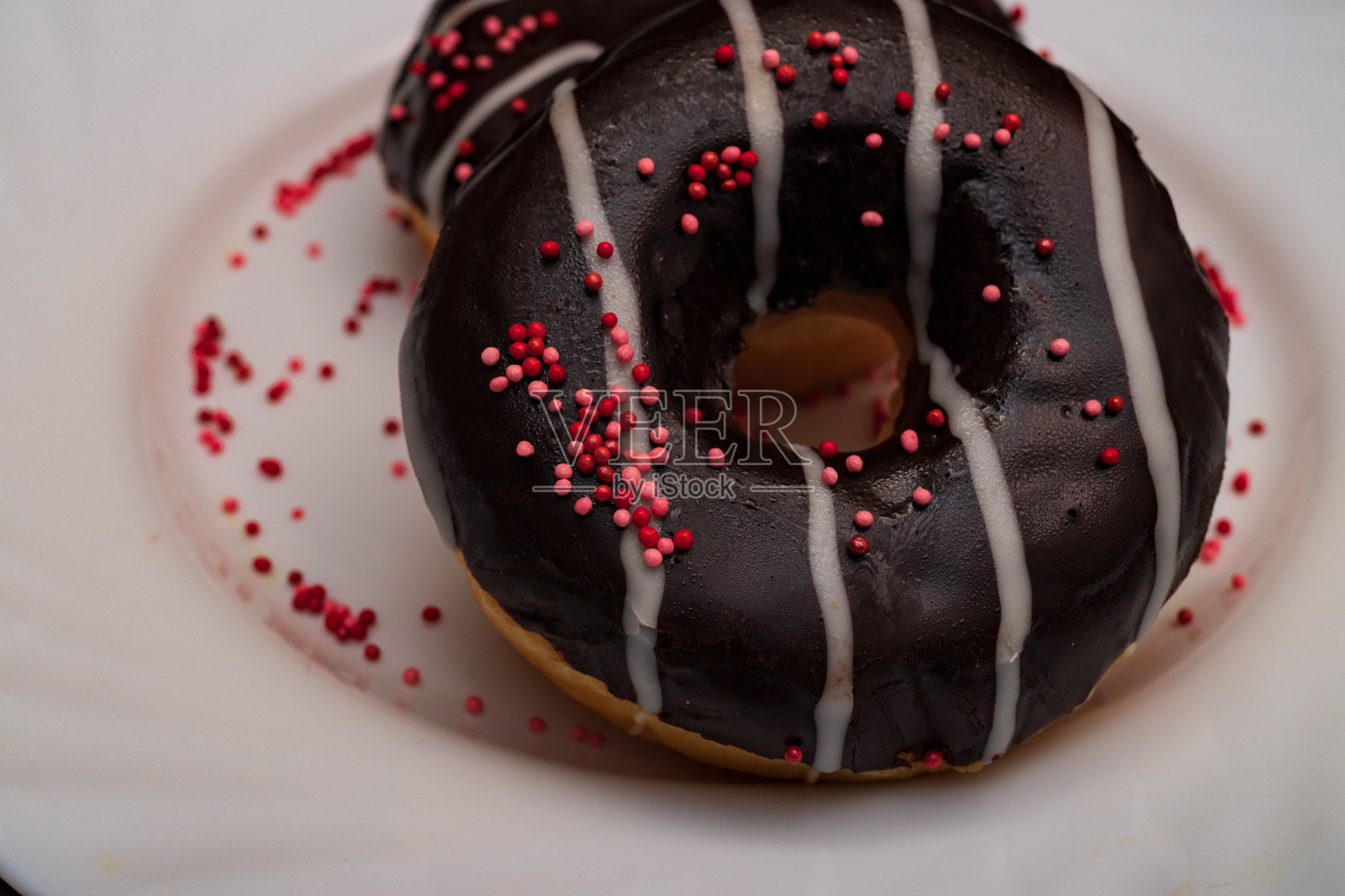 白色盘子里放着巧克力甜甜圈,上面撒着糖屑照片摄影图片