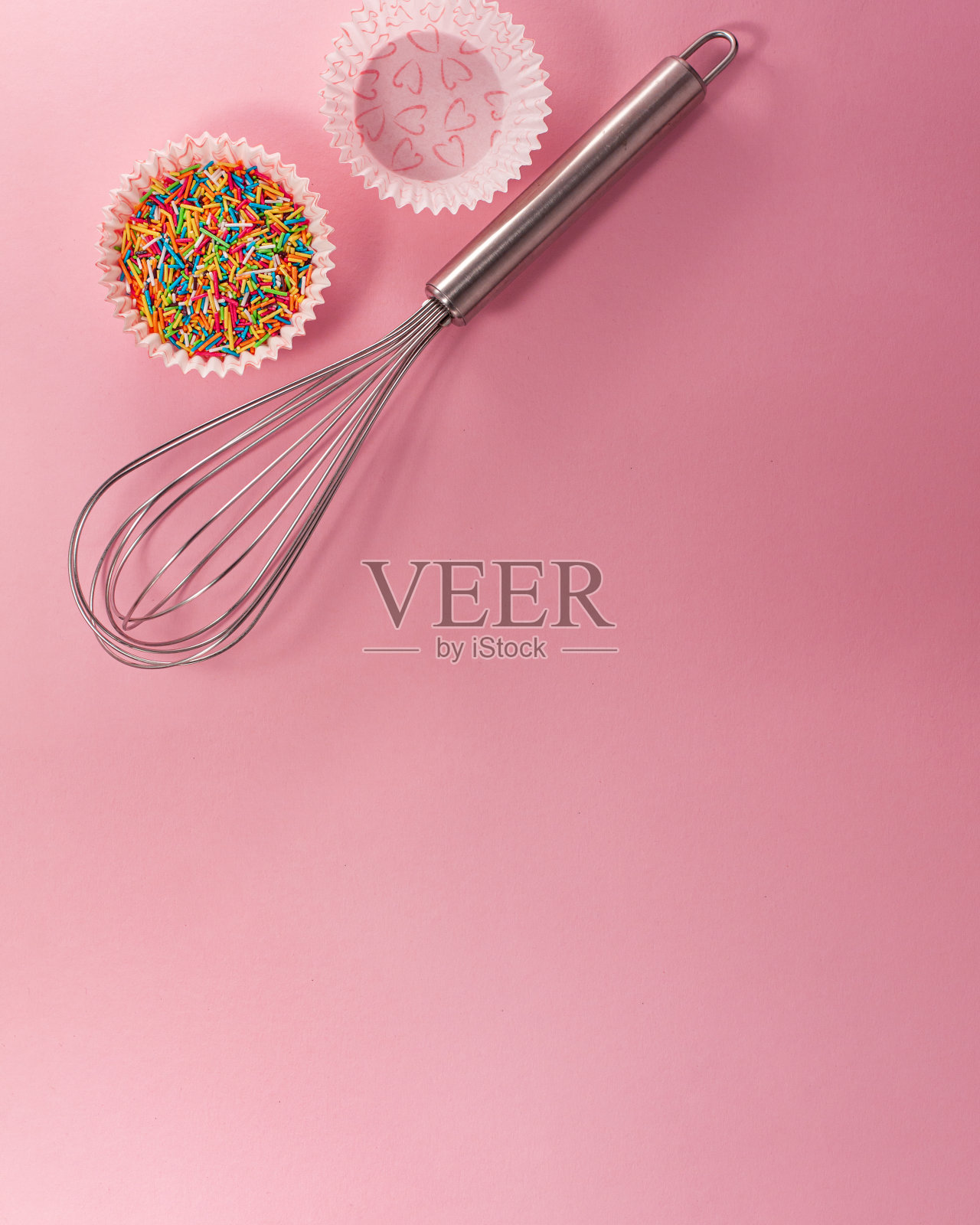 纸杯蛋糕衬垫与彩色糖内部搅拌从上面的平面俯视图。糖果烹饪概念与复制空间在明亮的粉红色纸的背景。全国烹饪的一天。照片摄影图片