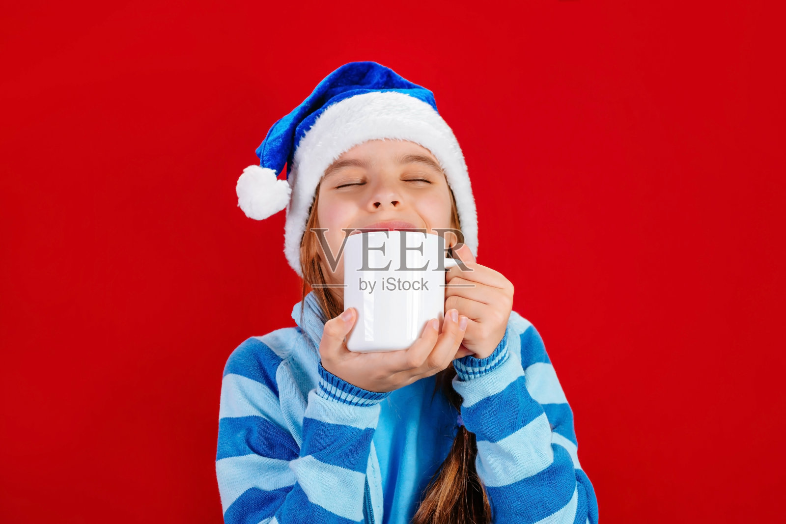 一个戴着蓝色圣诞帽的小女孩拿着一个白色的杯子模型。圣诞节的概念,品牌。照片摄影图片