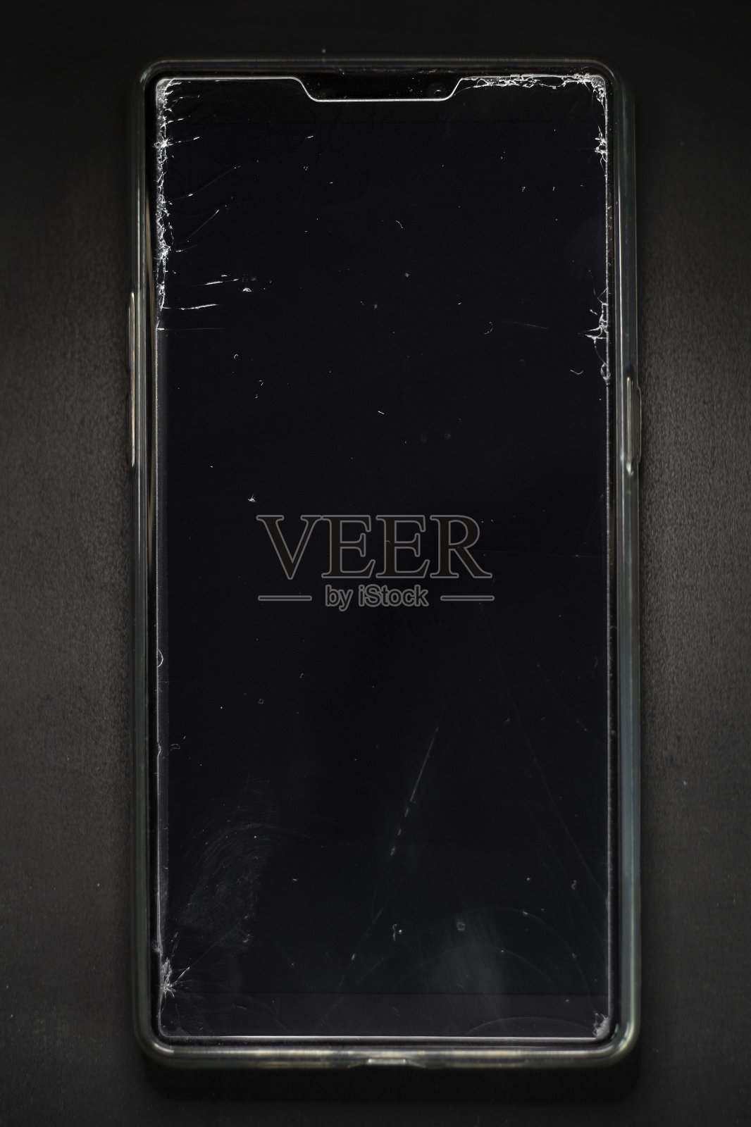 一个破碎的智能手机屏幕上的裂痕。黑暗背景下的手机保护膜损坏。照片在软焦点在高倍放大。照片摄影图片