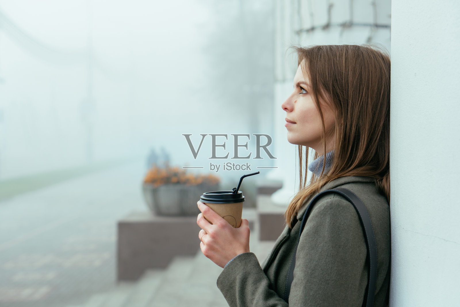 美丽的女孩坐在雾蒙蒙的街道上,手里拿着咖啡,用吸管喝着咖啡照片摄影图片