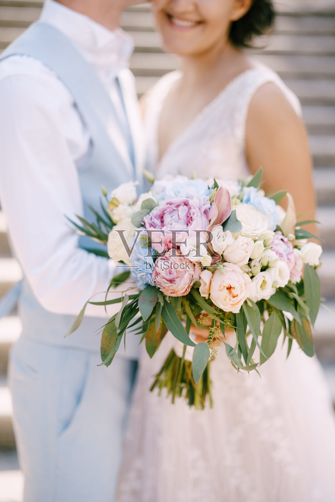 在Prcanj,新娘拿着玫瑰和牡丹的花束,新郎拥抱站在古老的楼梯上,特写照片摄影图片