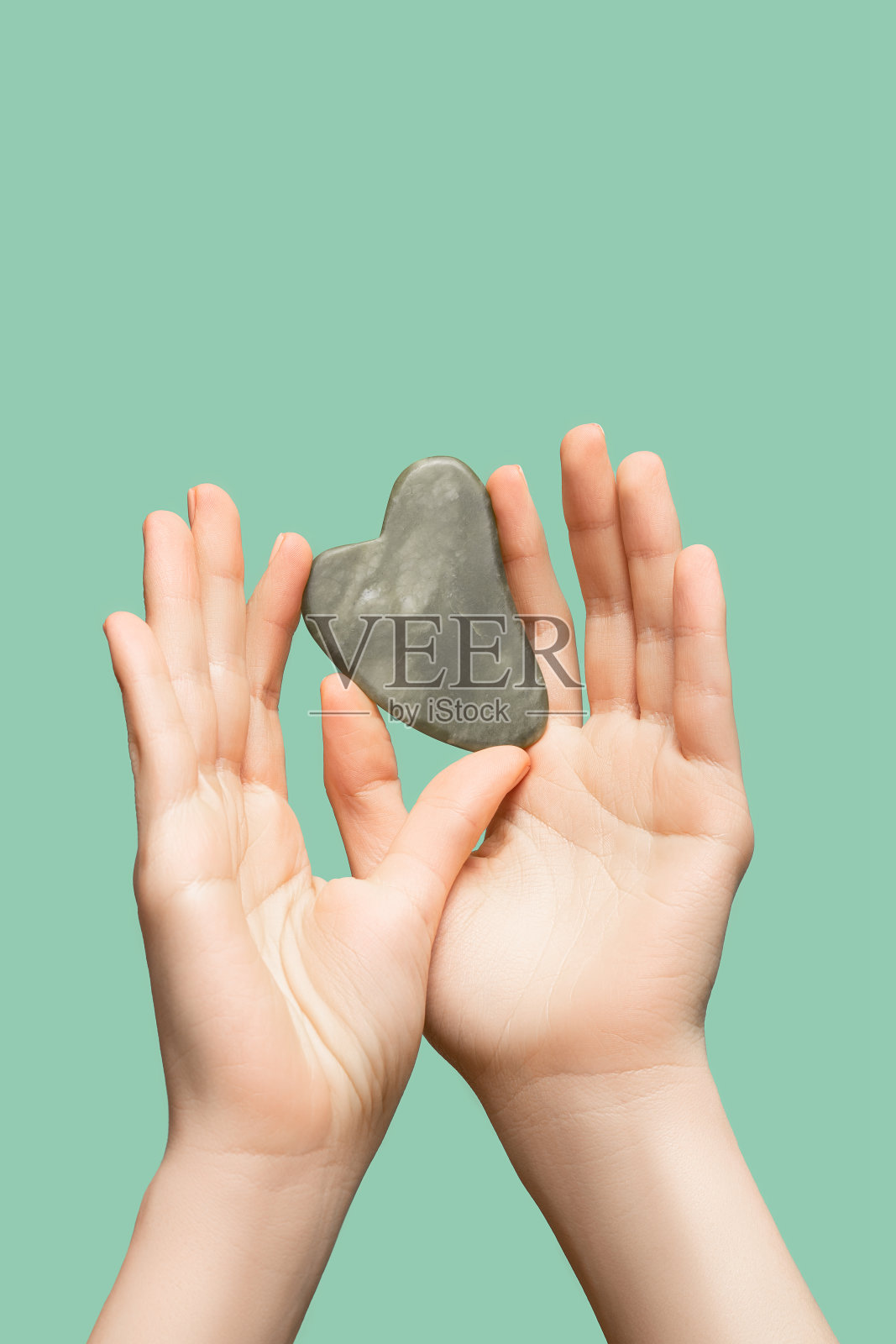 女性模特手拿青玉刮刀在绿色底色上。Spa身体护理工具。美容护理刮痧石刮刀。副本的空间。照片摄影图片