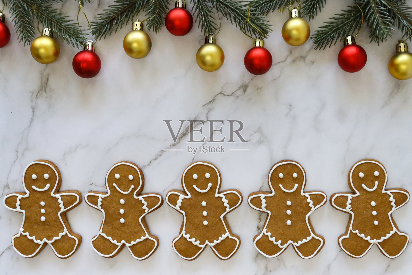 这是一排自制的姜饼人饼干,上面覆有白色的皇家糖霜,大理石效果的背景,云杉针叶和红色和金色的小玩意的框架照片摄影图片