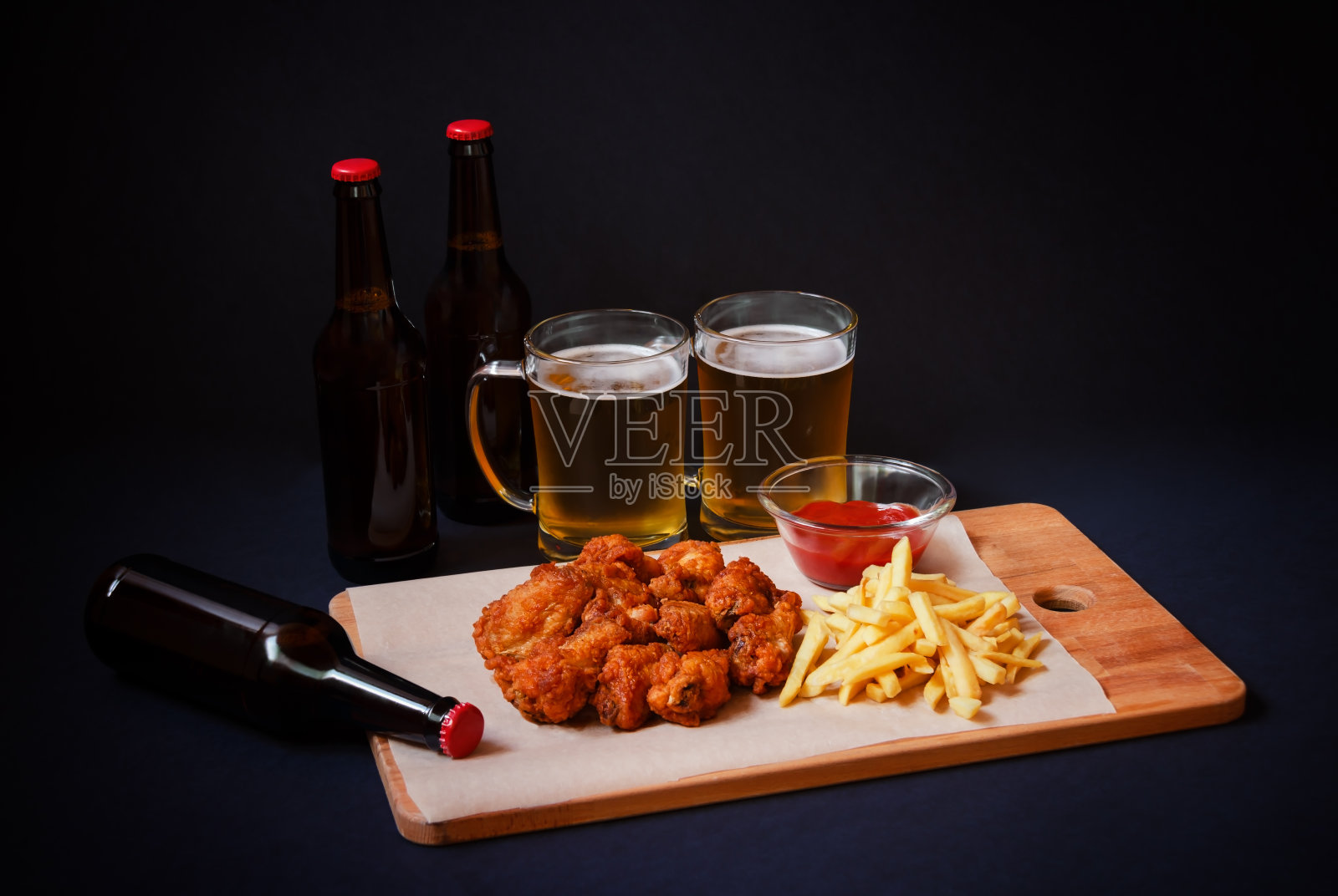 鸡翅和薯条放在砧板上,啤酒和啤酒的黑色背景。照片摄影图片