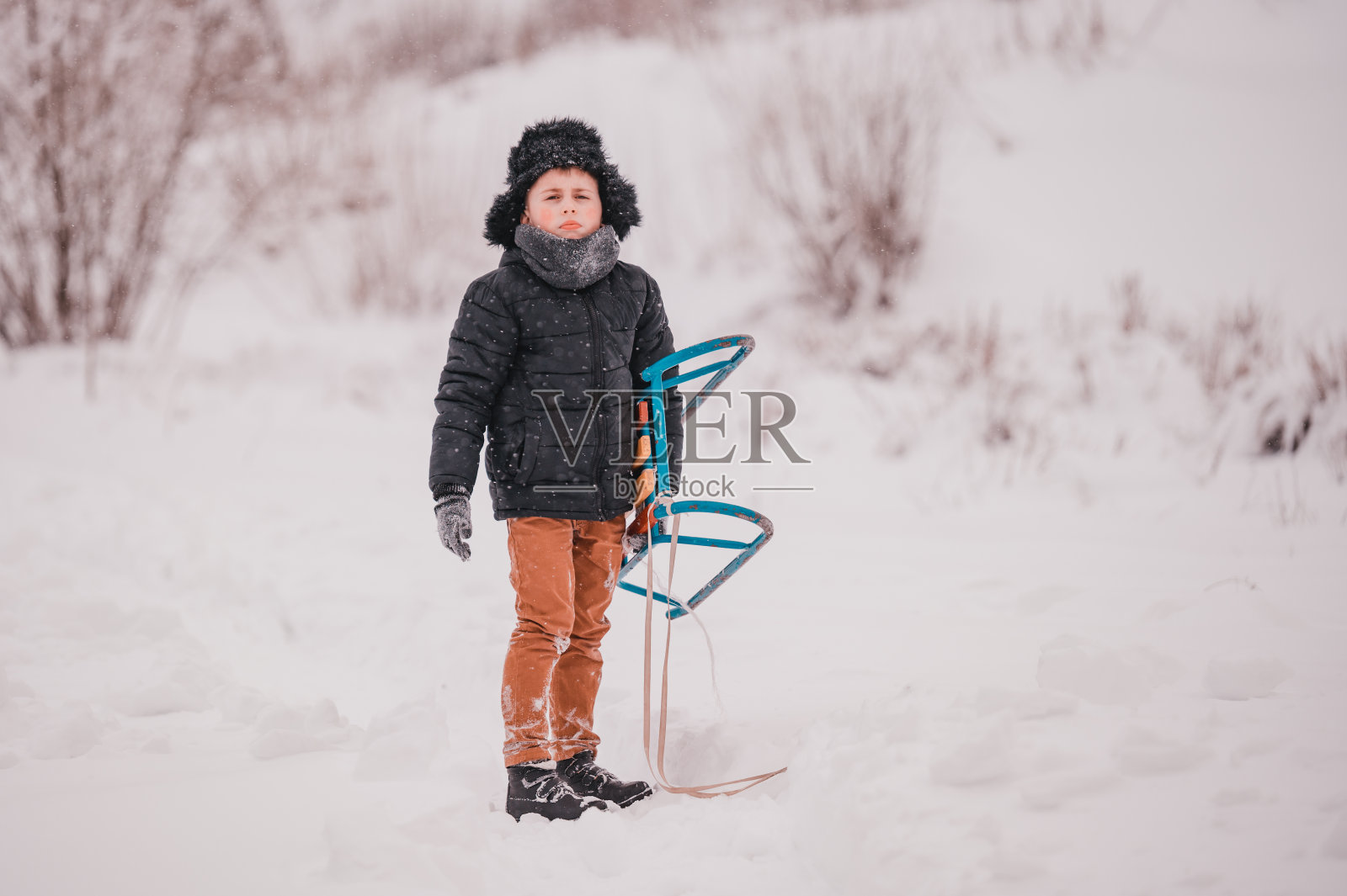 这家伙正坐着雪橇从山上滑下来,院子里下雪的时候,冬天很开心。照片摄影图片