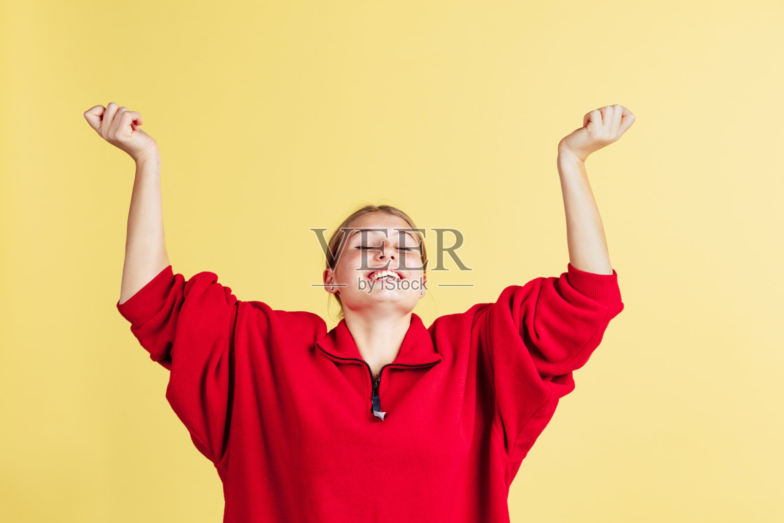 一个满脸雀斑的可爱女孩微笑着举起手,欣喜地站在黄色工作室的背景上。情绪的概念,照片摄影图片