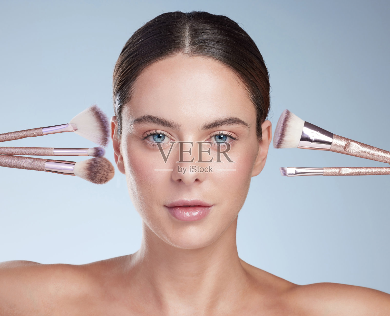 工作室肖像的一个有吸引力的年轻女子摆姿势与各种化妆刷对灰色的背景照片摄影图片