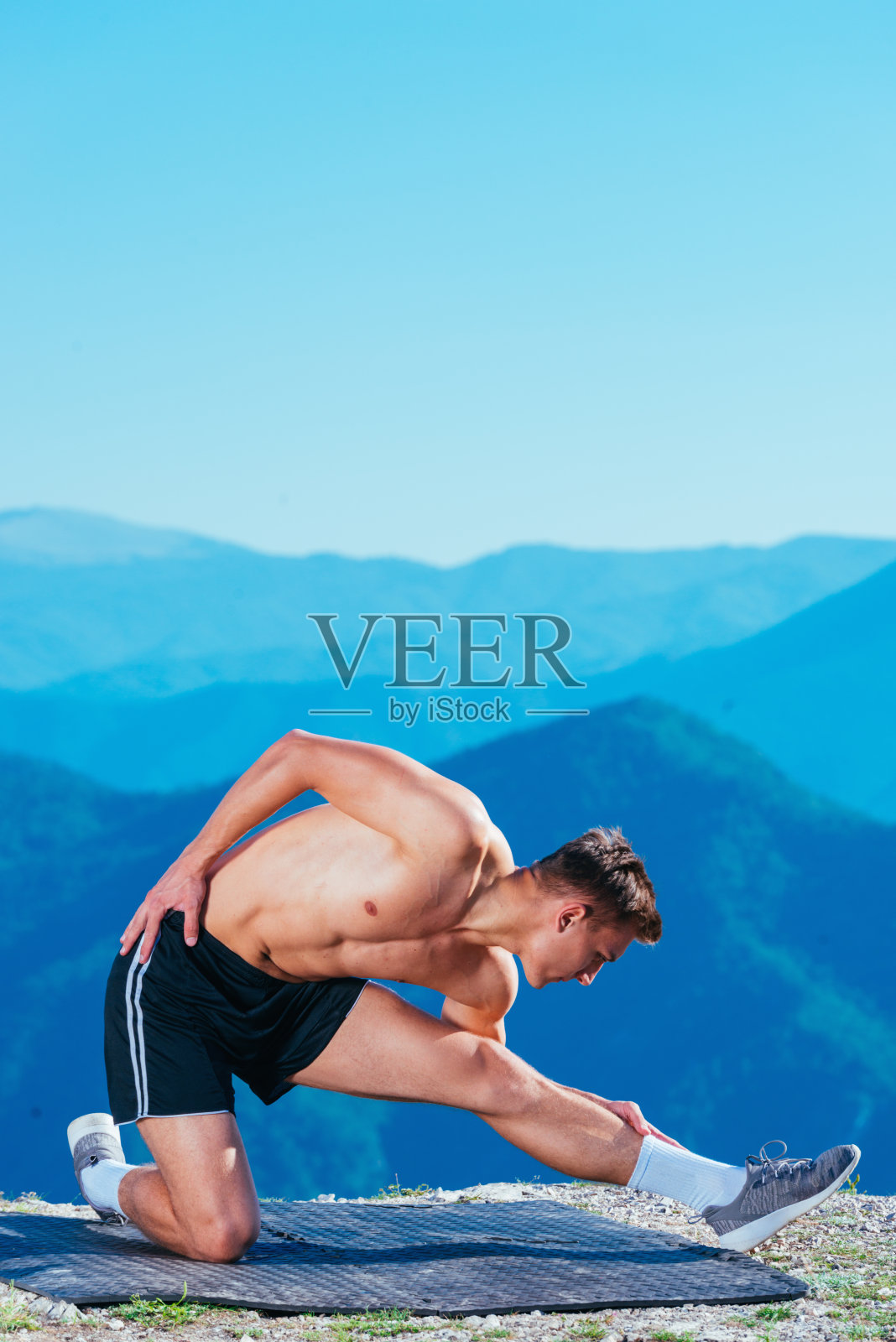 英俊的运动员(运动员)在山顶伸展身体准备锻炼,山上有令人惊叹的风景。照片摄影图片