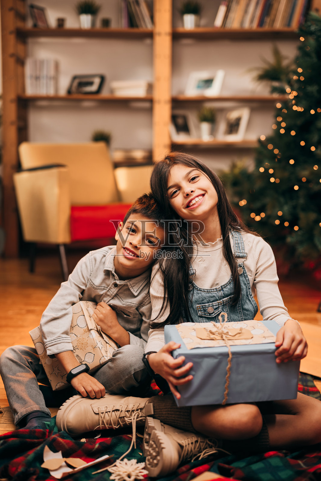 圣诞前夜,哥哥和姐姐在家里挨着坐在地板上,手里拿着圣诞礼物。圣诞节及新年照片摄影图片