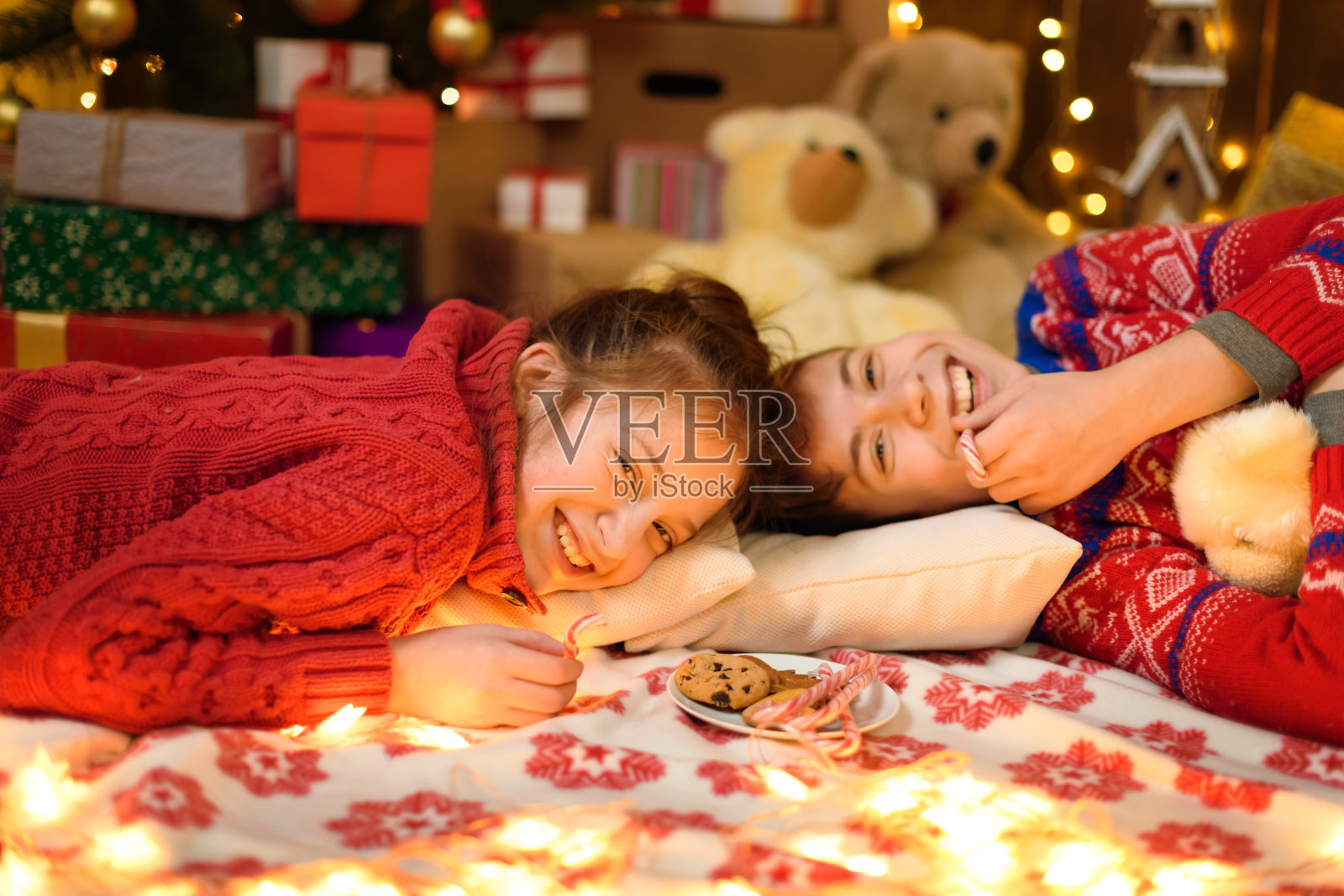 男孩和女孩的肖像在新年或圣诞节装饰。他们撒谎,吃糖果和饼干。节日彩灯、礼物和玩具装饰的圣诞树。照片摄影图片