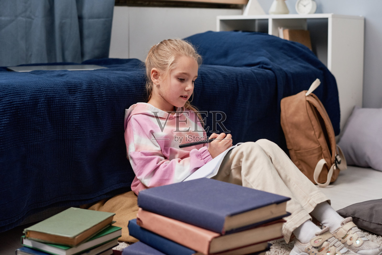 金发女孩穿着带有抽象图案的连帽衫坐在床上,阅读笔记,同时准备学校考试照片摄影图片