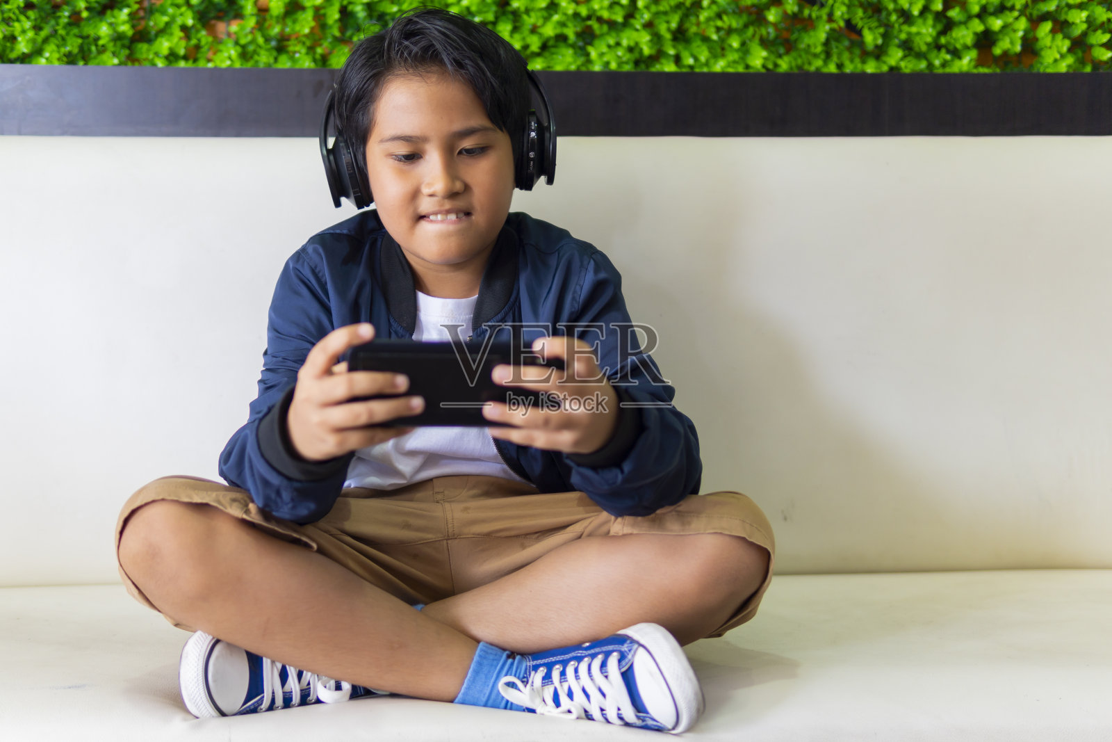 小男孩戴着耳机用智能手机玩游戏照片摄影图片