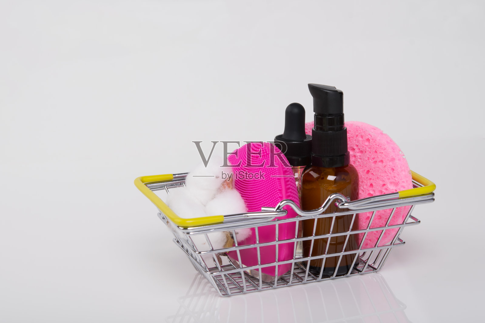 在白色的背景上,有一个铁制的篮子,里面放着按摩油和洗脸用的海绵照片摄影图片