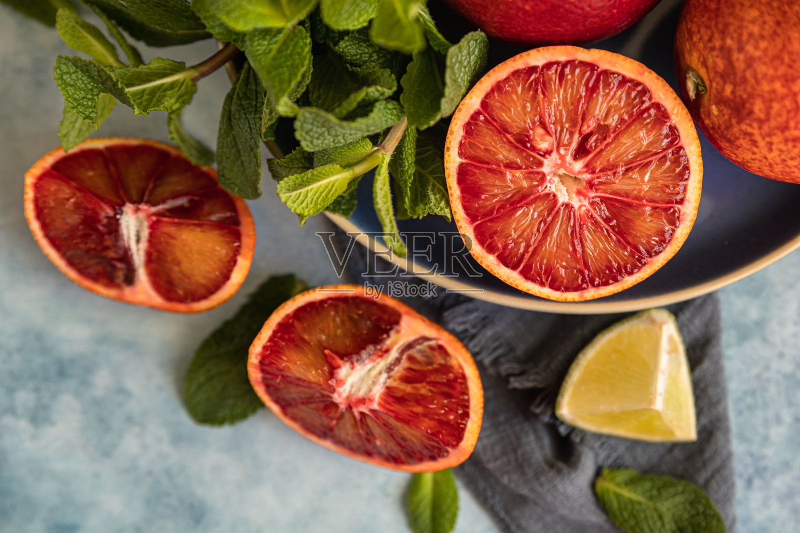 整只切一半的纯正西西里橙子,酸橙和薄荷放在蓝色混凝土的背景上。前视图。照片摄影图片