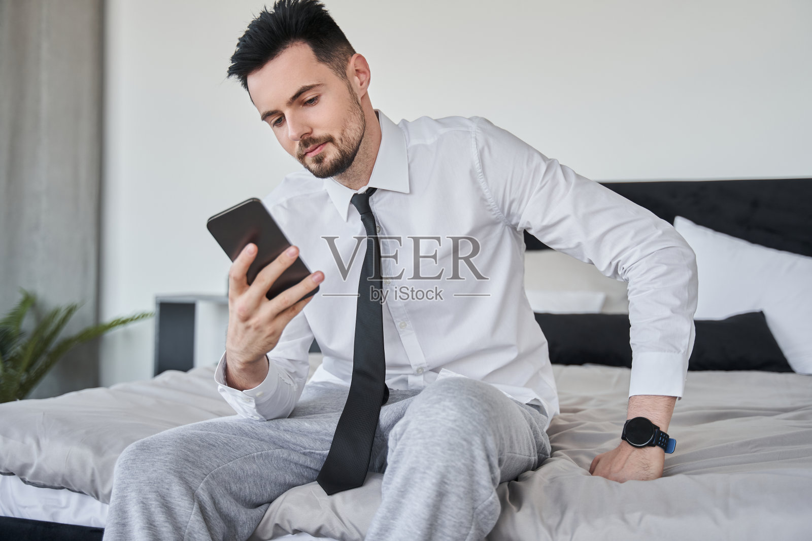 男人坐在床上,一边看智能手机屏幕,一边查看电子邮件照片摄影图片