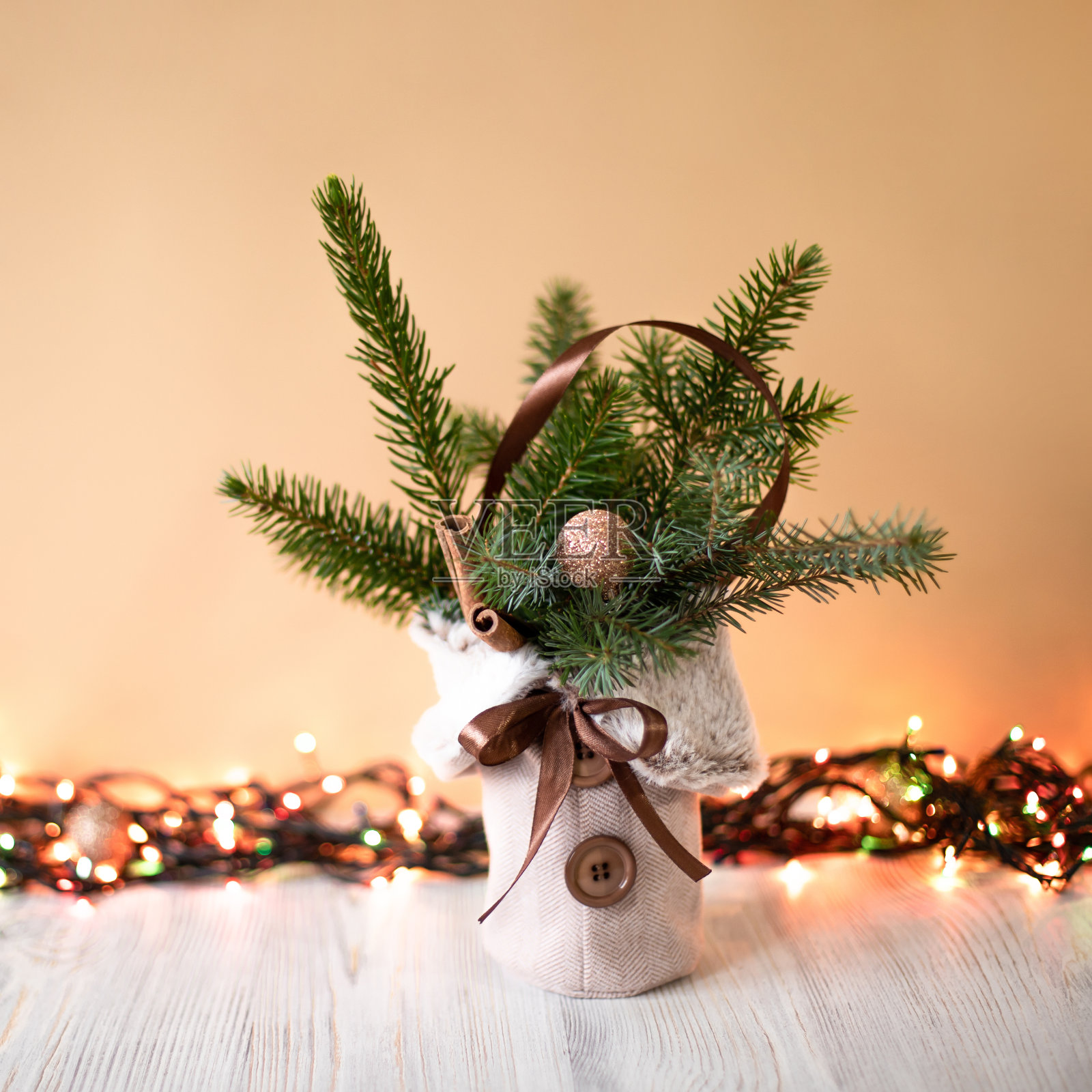 圣诞装饰品在金木背景与圣诞灯花环。圣诞冷杉树,肉桂棒和球组成。有人造毛皮和针叶树枝的纺织品花瓶。前视图。照片摄影图片