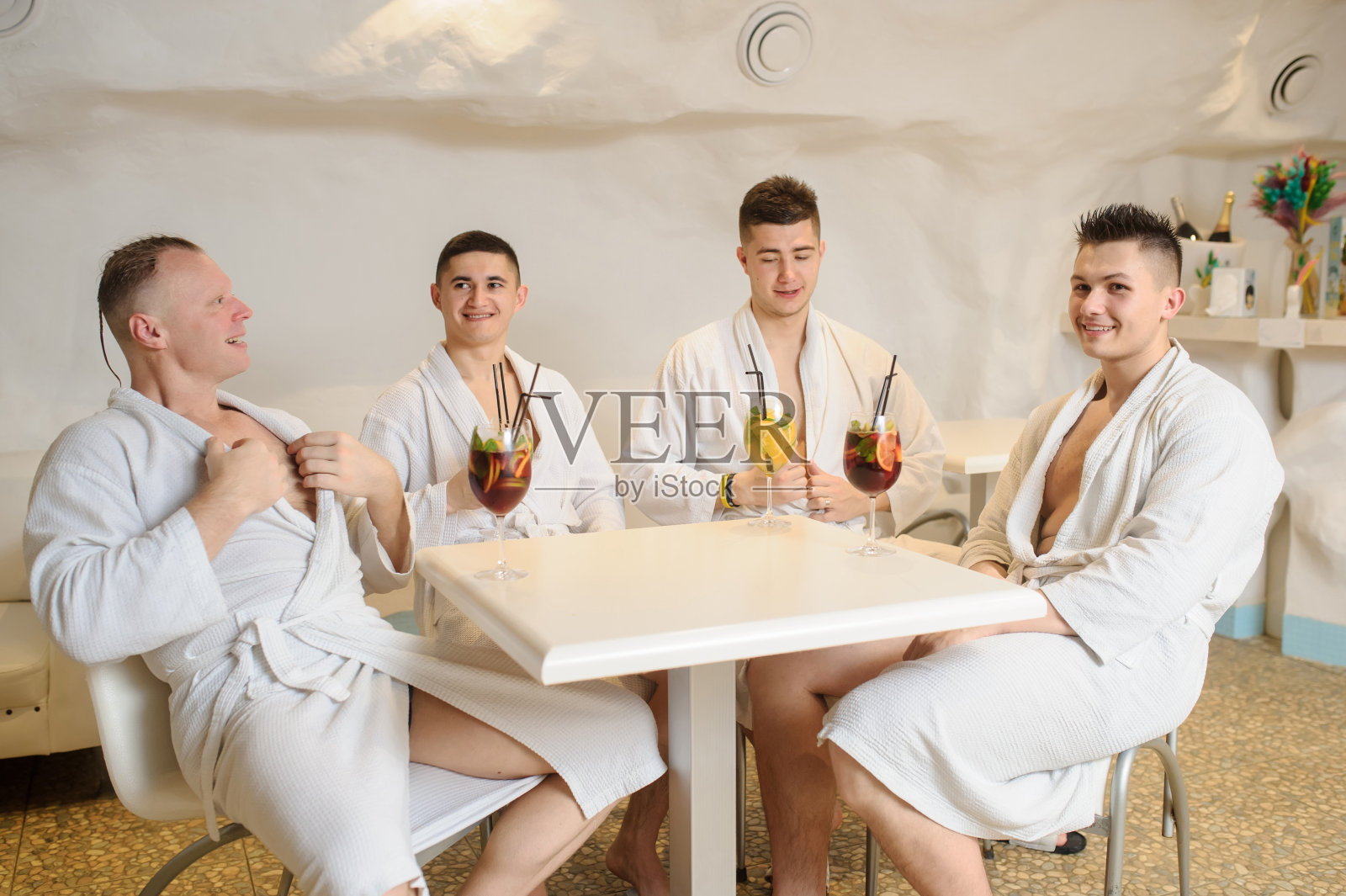 穿着白大褂的男人围坐在桌旁,喝着桑格利亚汽酒和柠檬水照片摄影图片