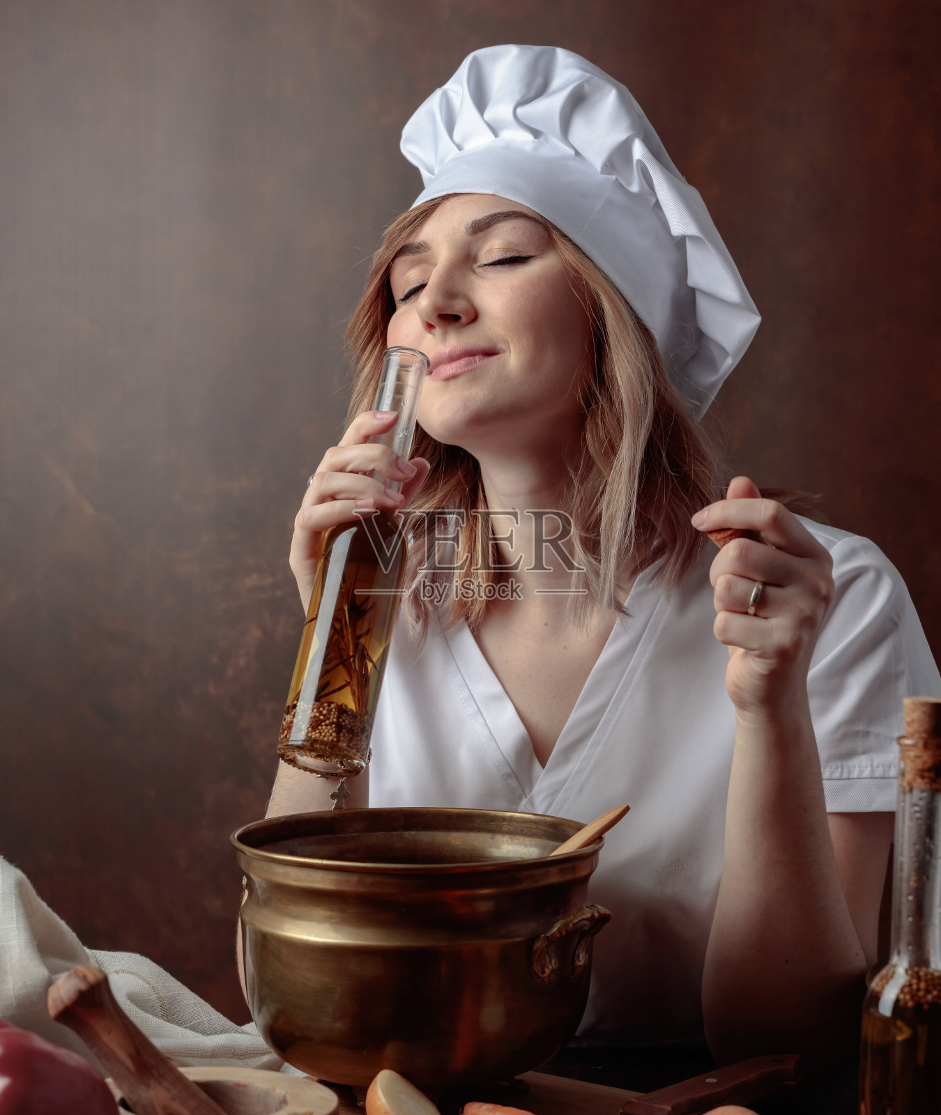 穿着厨师制服的年轻女子手里拿着小瓶橄榄油。照片摄影图片