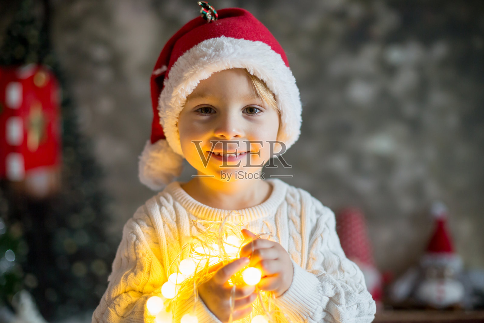 漂亮的蹒跚学步的男孩,拿着圣诞灯线,看着相机照片摄影图片