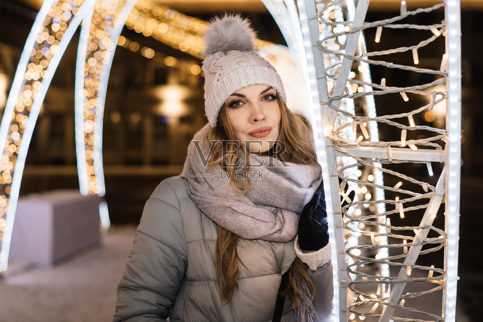 漂亮的年轻女子穿着暖和的衣服,旁边是圣诞城市装饰上美丽的发光的灯。模糊的灯光照片摄影图片