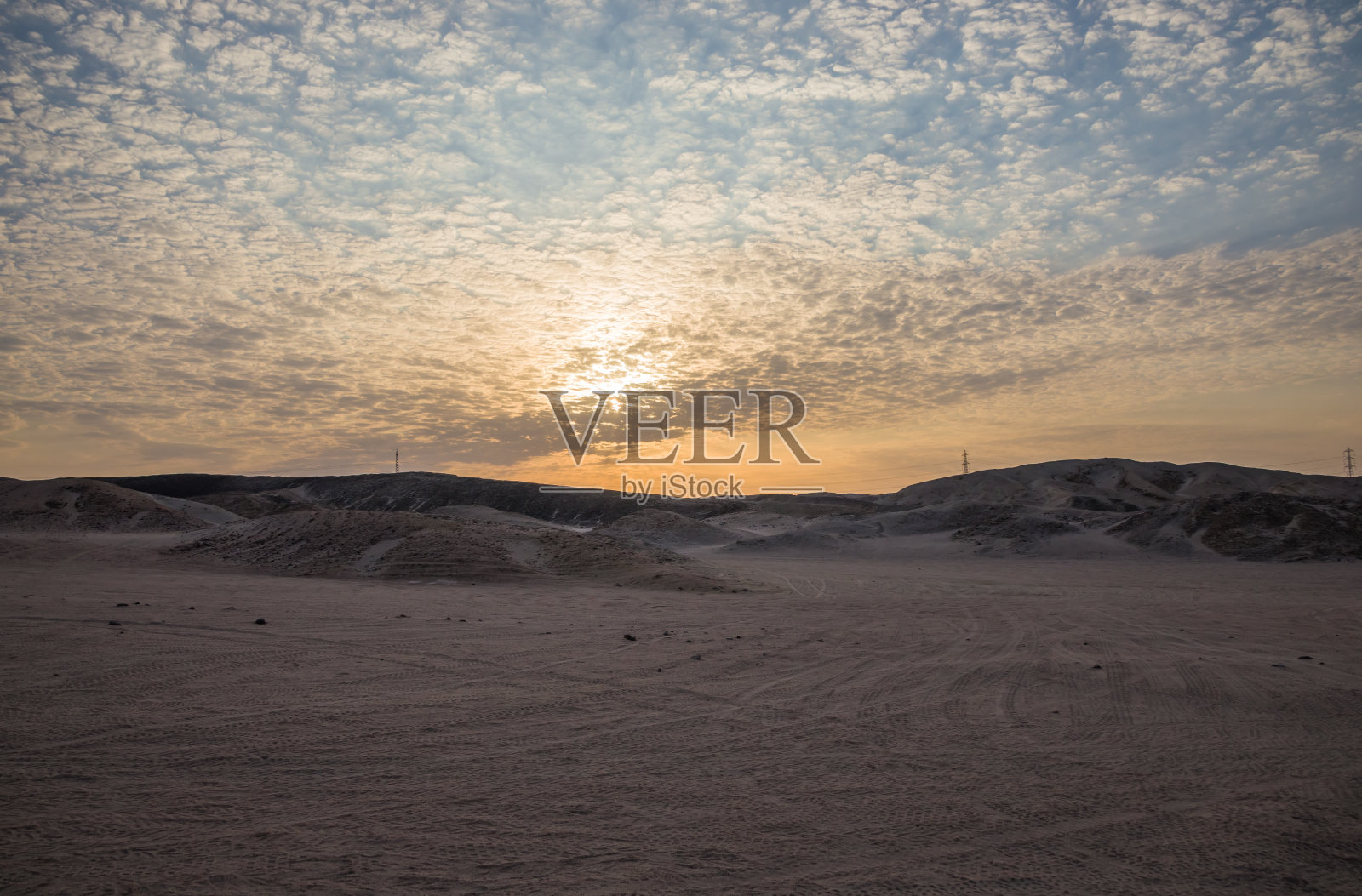 日落后的沙漠山脉,埃及的沙地在前景,岩石山脉在背景。日落时天空上的小云。照片摄影图片