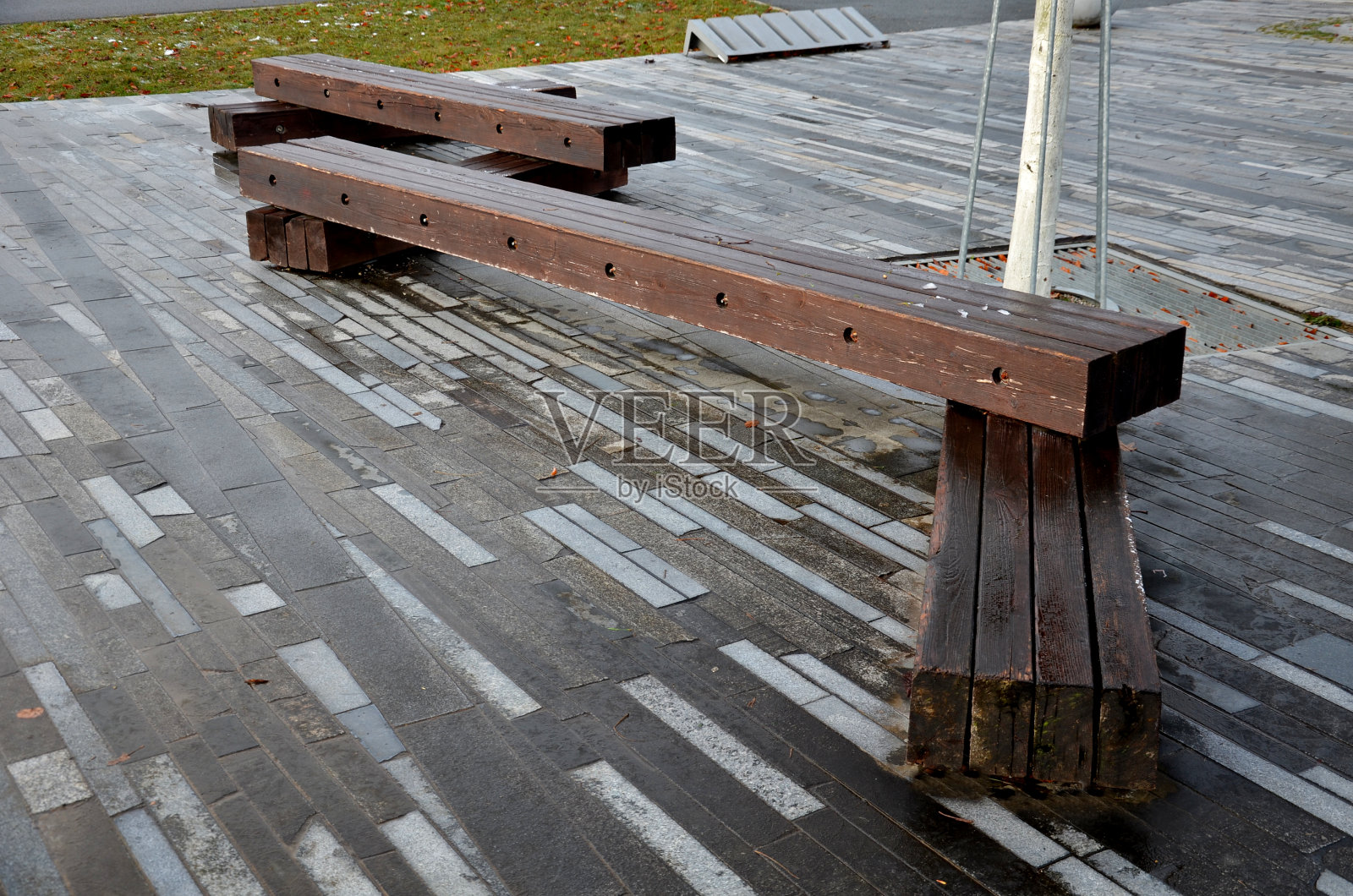 公园里的木制露台和棕色的螺丝固定的长凳把zig一个接一个地放回去。这些长椅是一个挨着一个的。固定在金属格栅上的树照片摄影图片