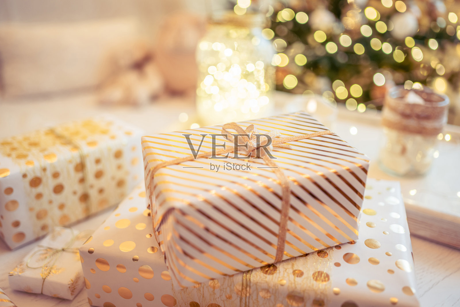 圣诞树附近的桌子上放着许多手工包装的礼品盒,在金色的灯光、发光的花环和蜡烛中。软焦点照片摄影图片