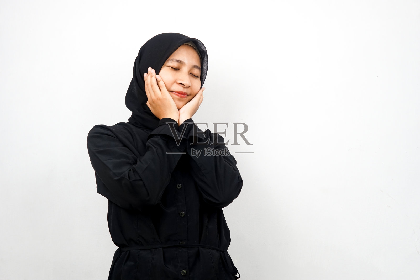 在白色背景下微笑,双手托腮,感觉舒适的年轻亚洲穆斯林女性照片摄影图片