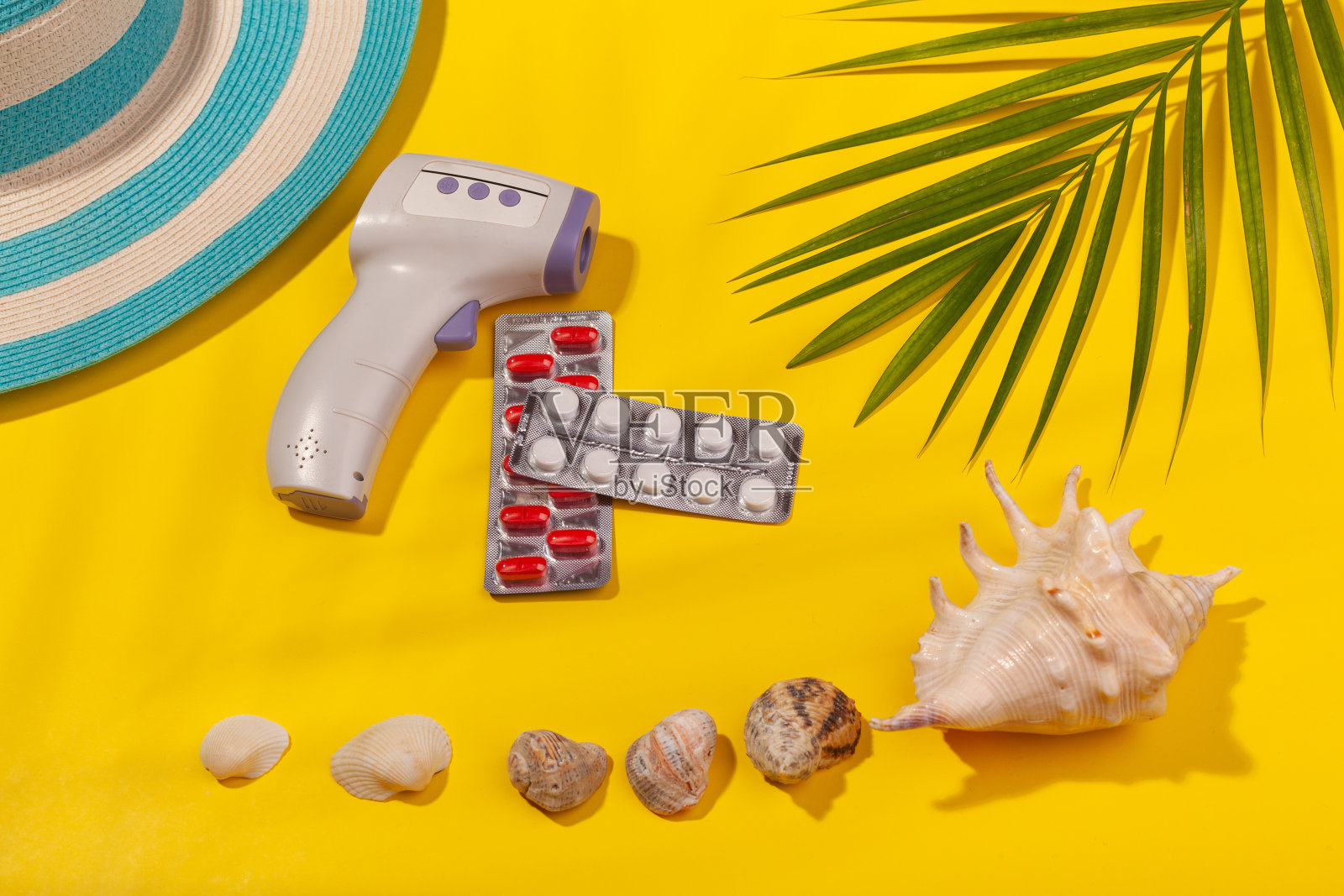 俯视图在红外温度计,白色和红色丸在水泡包装,蓝色的帽子,贝壳,棕榈叶在黄色的背景。海滩度假、海上旅游、温暖阳光夏日的概念。在海上度假准备生病的概念。广告空间照片摄影图片