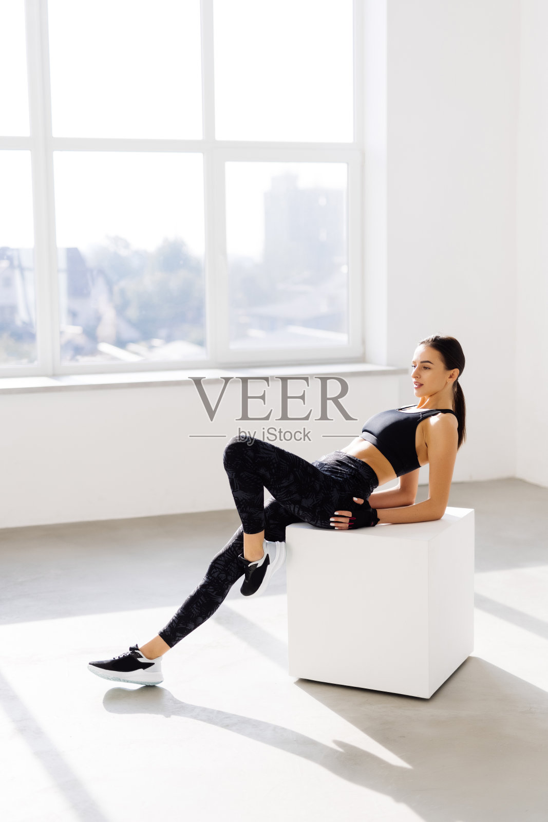 健身年轻女子在健身后坐在一个盒子上。女运动员在健身房锻炼后休息。照片摄影图片