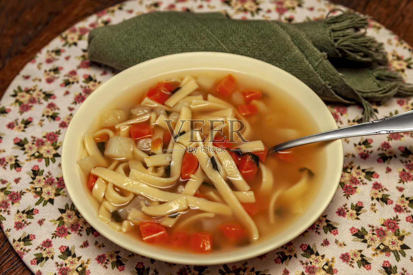 从以上。木桌上有图案的餐具柜上放着一盘蔬菜汤和面条。照片摄影图片