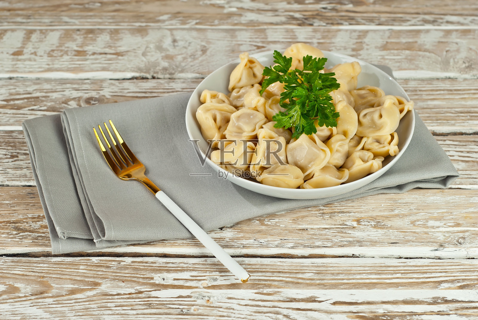 在一张破旧的桌子上,一个白色盘子里的饺子。饺子与黄色的面团接近。食物在白板的背景上。照片摄影图片