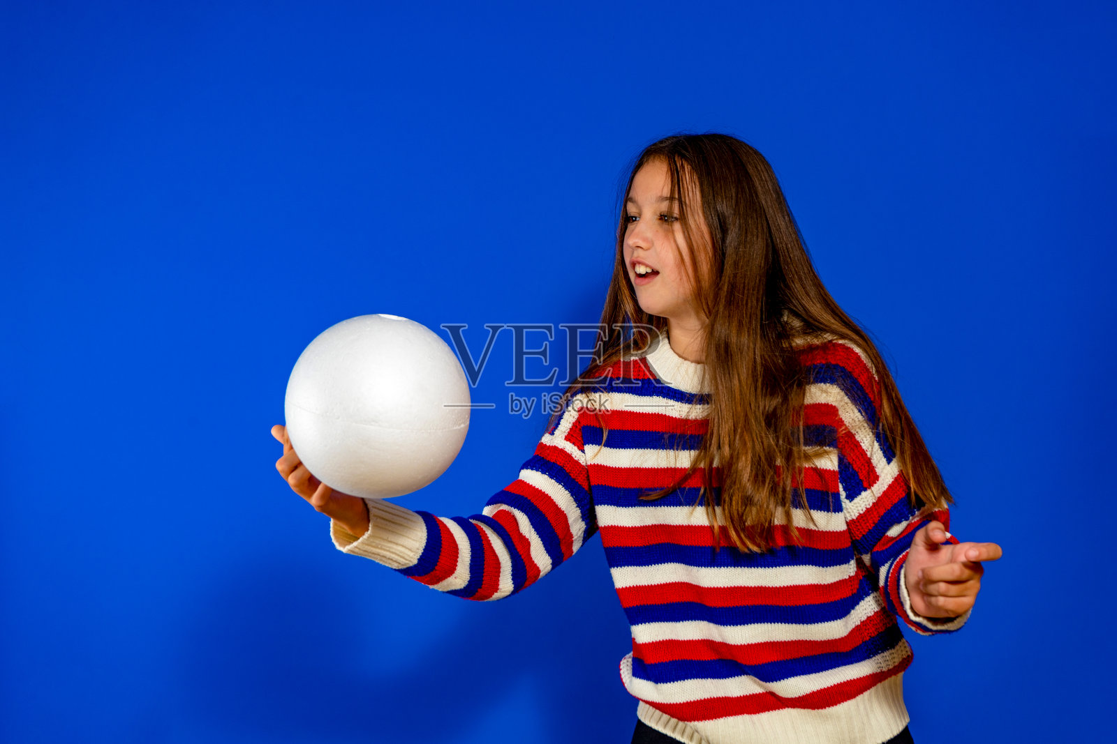 孩子们的真正的情感。一个小女孩抓着一个孤立在蓝色背景上的球照片摄影图片