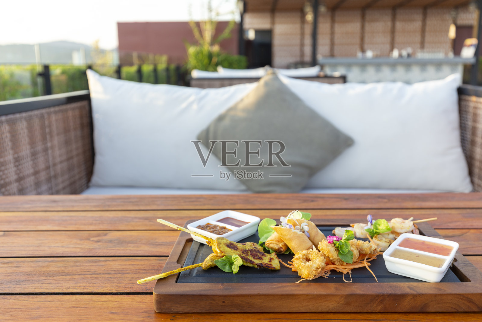 轻餐或小吃的木桌与沙发和枕头座位在阳台在日落时分与晴朗的天空,复制空间的文本照片摄影图片