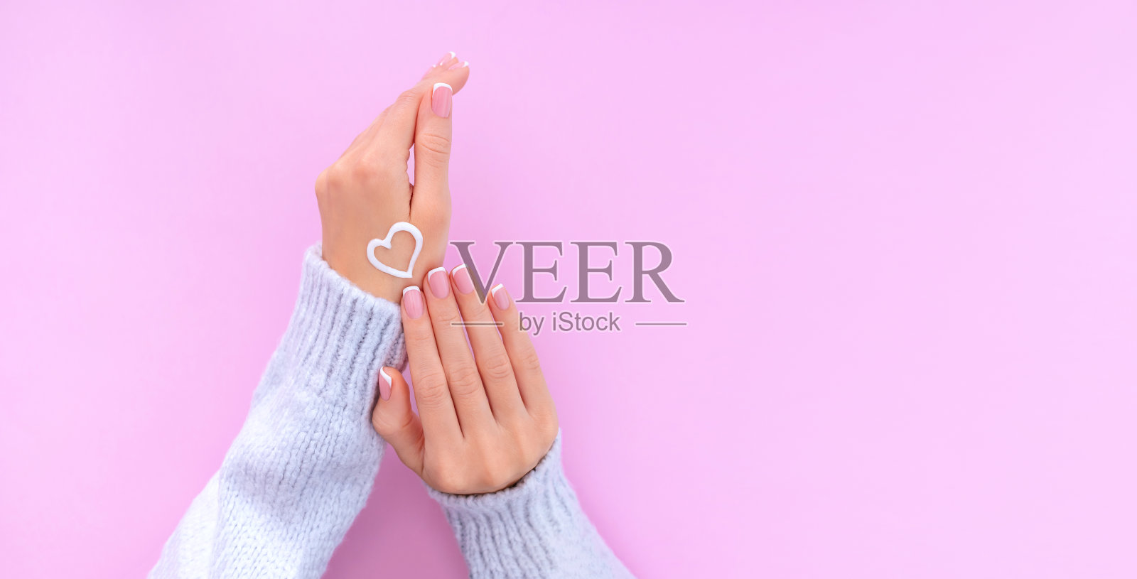 女性的手与法国美甲在粉红色的背景上保湿的手与手霜照片摄影图片