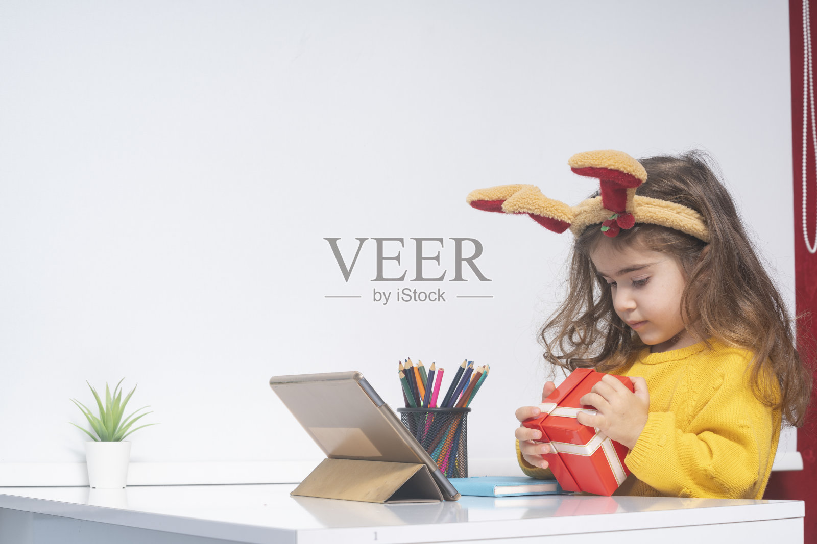 小女孩戴着驯鹿的鹿角,用数码平板电脑打开圣诞礼物盒照片摄影图片