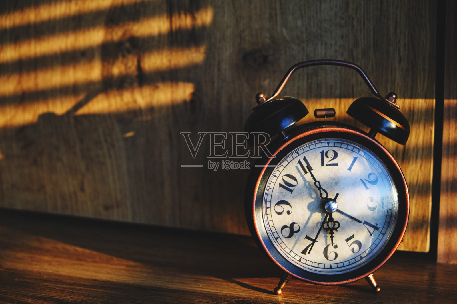 桌上的复古闹钟清晨透过卧室的百叶窗照射阳光。照片摄影图片