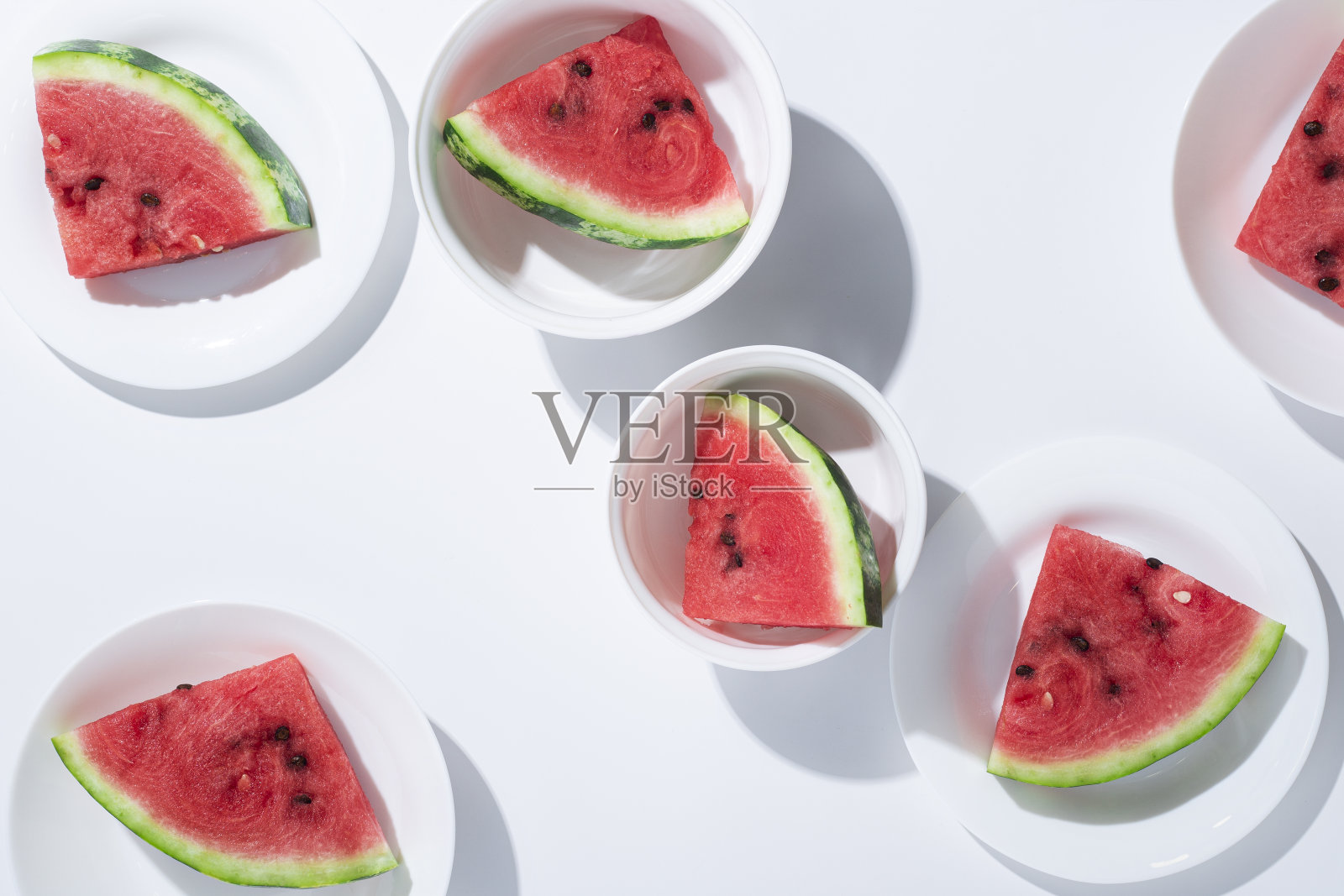 白色桌子上的白色盘子里放着成熟的西瓜片。俯视图,平铺照片摄影图片
