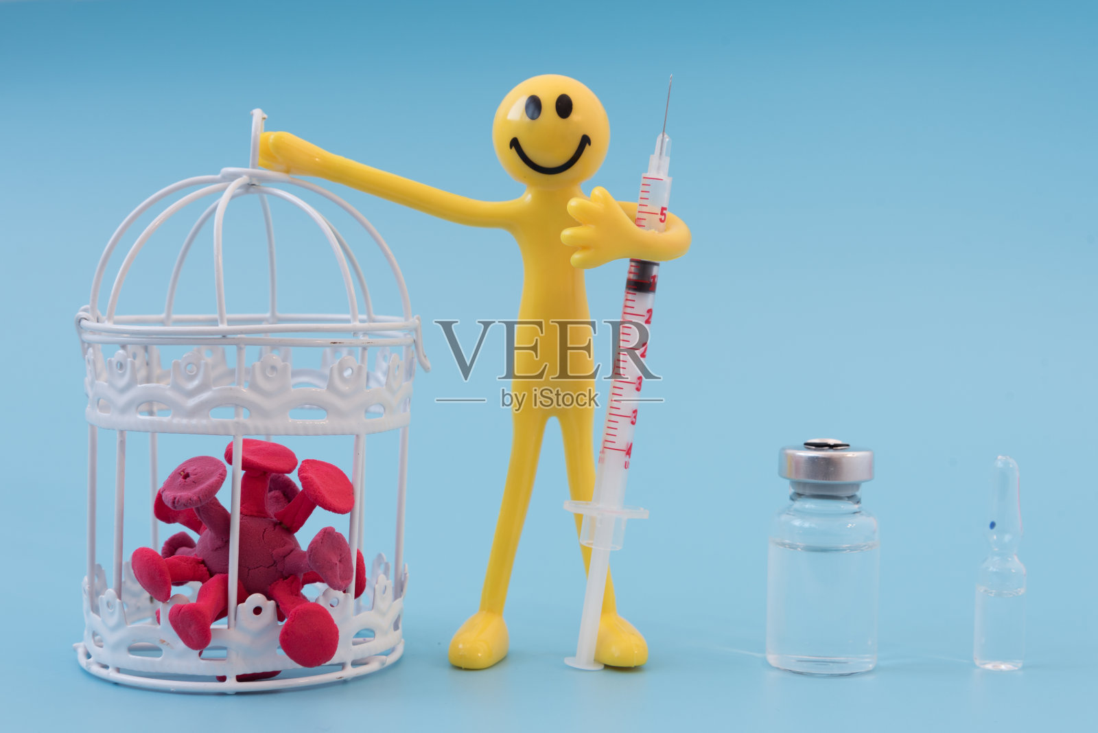 一个乐观的黄种人手里拿着一个装有冠状病毒的笼子。用疫苗或药物战胜大流行的概念。另一只手拿着注射器。附近有疫苗照片摄影图片