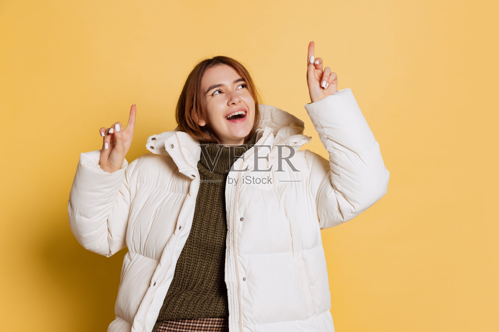 年轻快乐的女孩的肖像,学生穿着温暖的冬衣孤立在黄色的画室背景。照片摄影图片