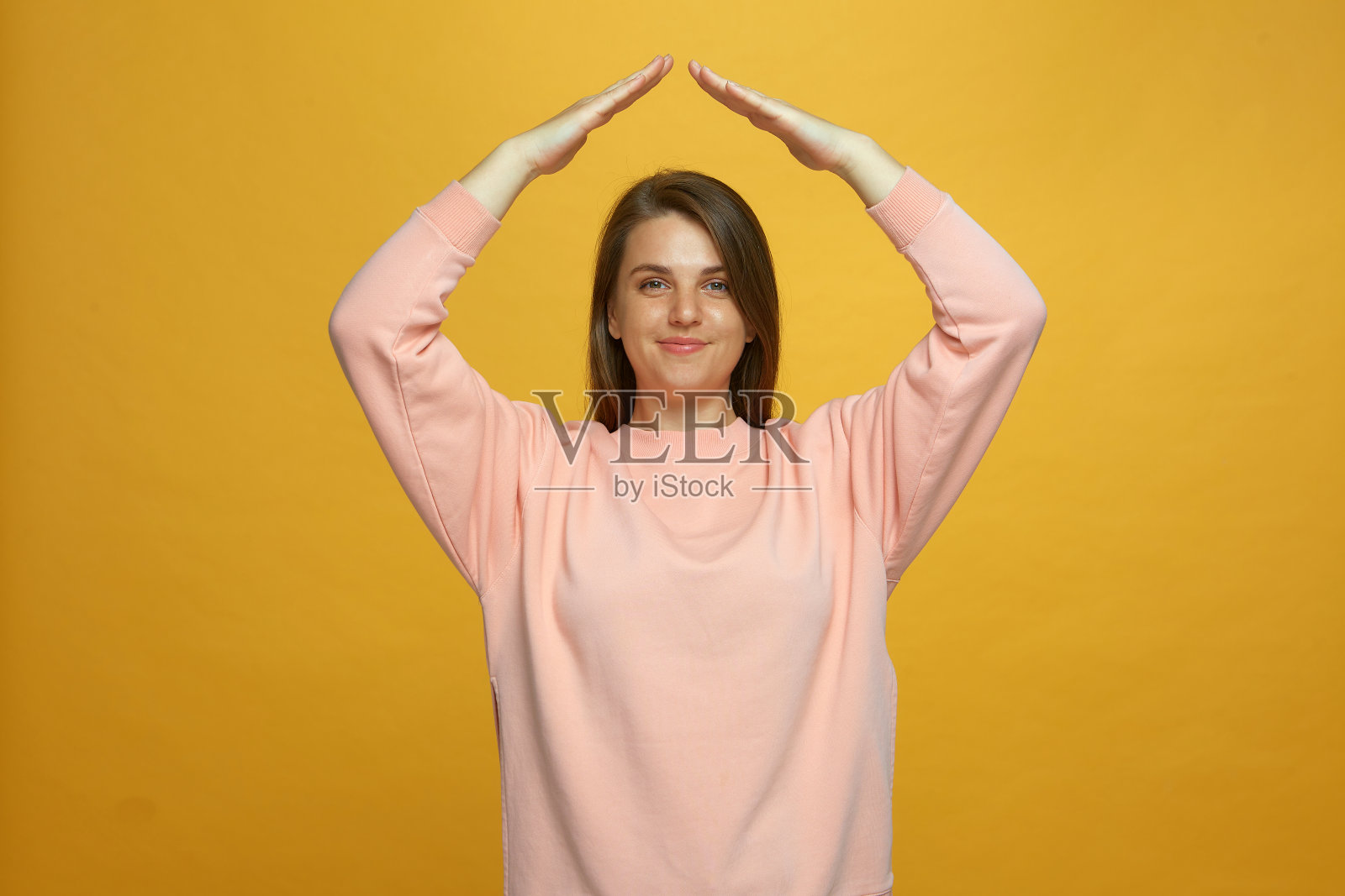 人寿保险。积极的年轻女孩展示了屋顶的姿态在头顶上感觉自己在安全的黄色背景照片摄影图片