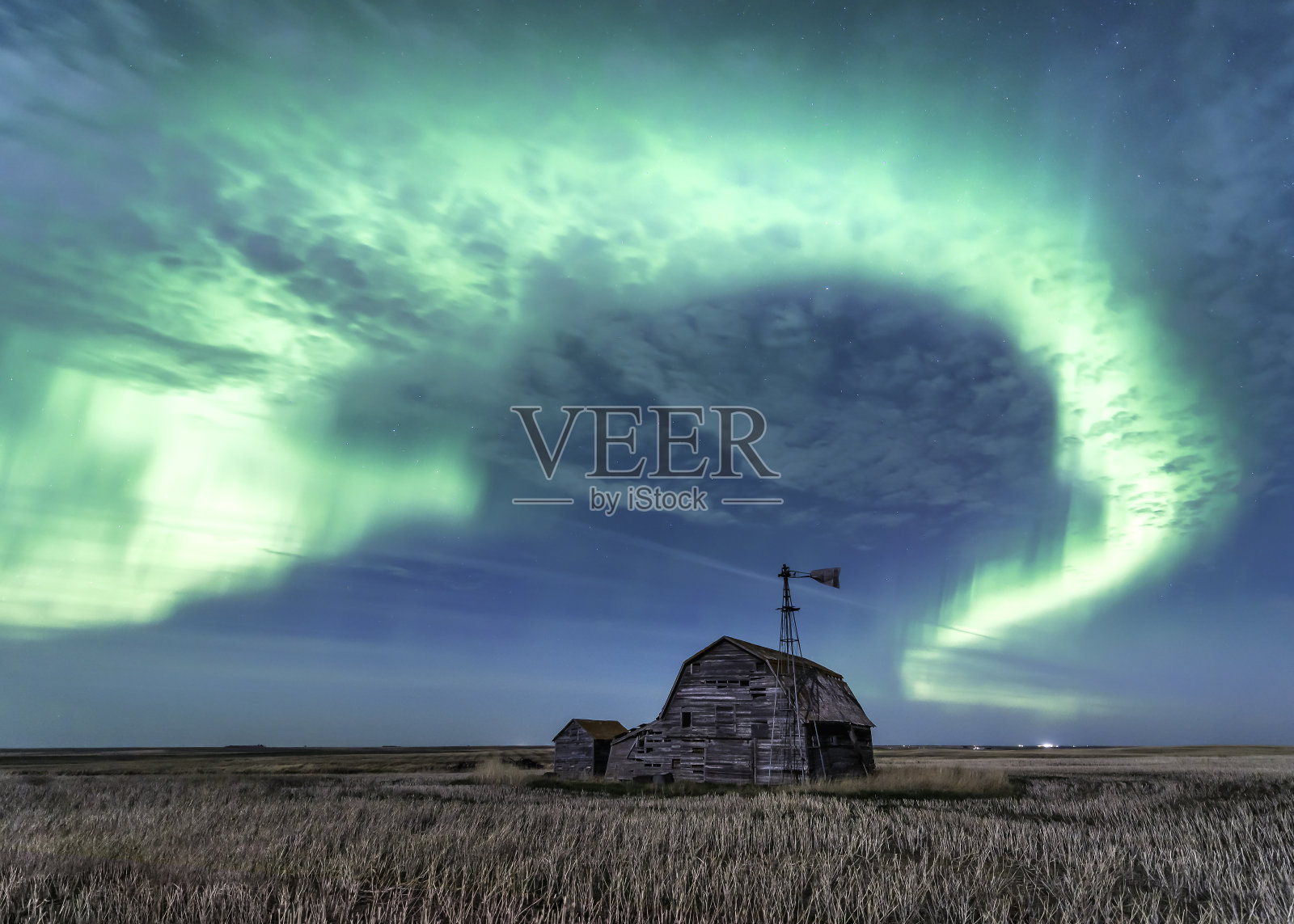 加拿大萨斯喀彻温省,明亮的北极光在老式谷仓、垃圾箱、风车和胡茬上旋转照片摄影图片