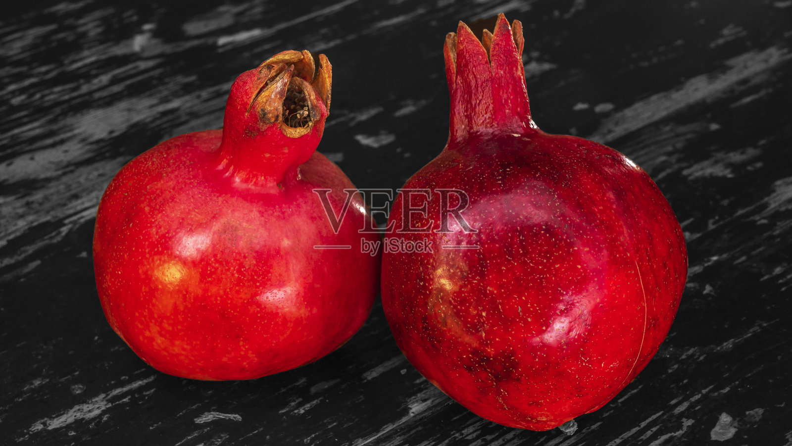 桌子上放着两个红石榴。两个成熟的石榴石在桌子上黑白木墙背景。照片摄影图片