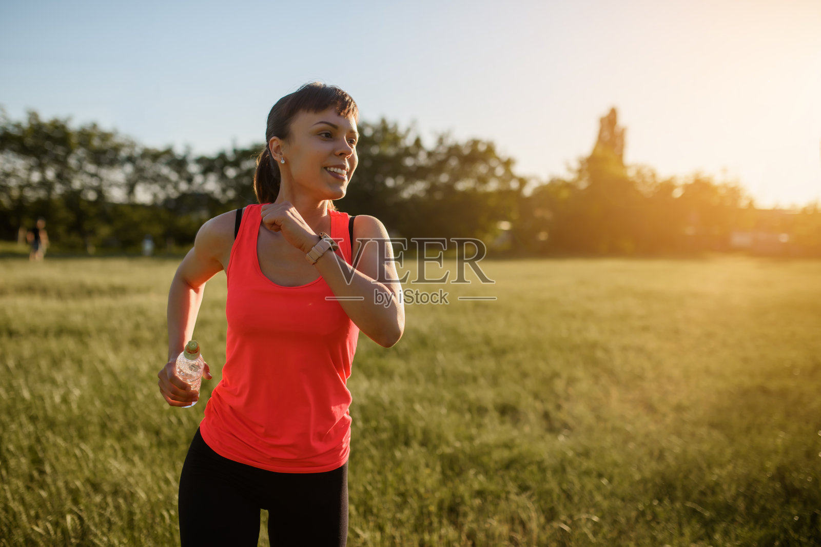 年轻美丽的女人正在运动,她在日落时分的大自然中,在草地上奔跑。照片摄影图片