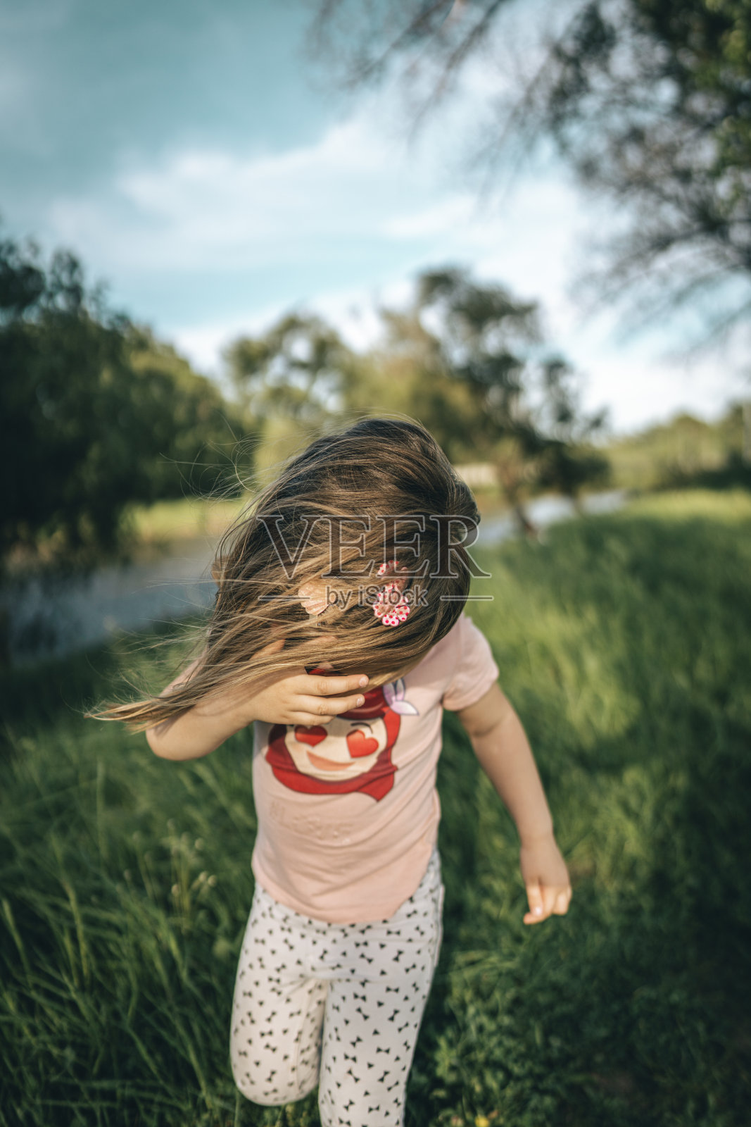 小女孩在刮风的日子穿过草地照片摄影图片