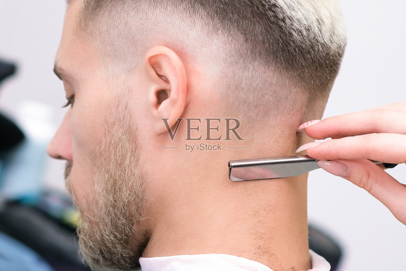 刮胡刀。理发过程的金发青年在理发店沙龙,理发店的概念照片摄影图片