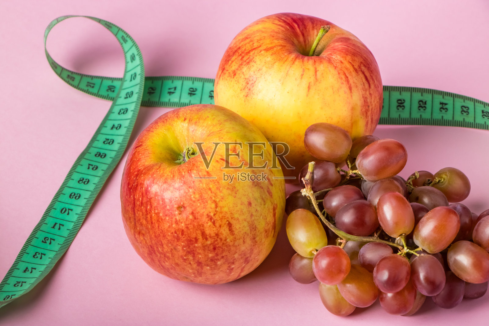 粉红色背景上的新鲜水果和卷尺。饮食和健康饮食的概念。照片摄影图片